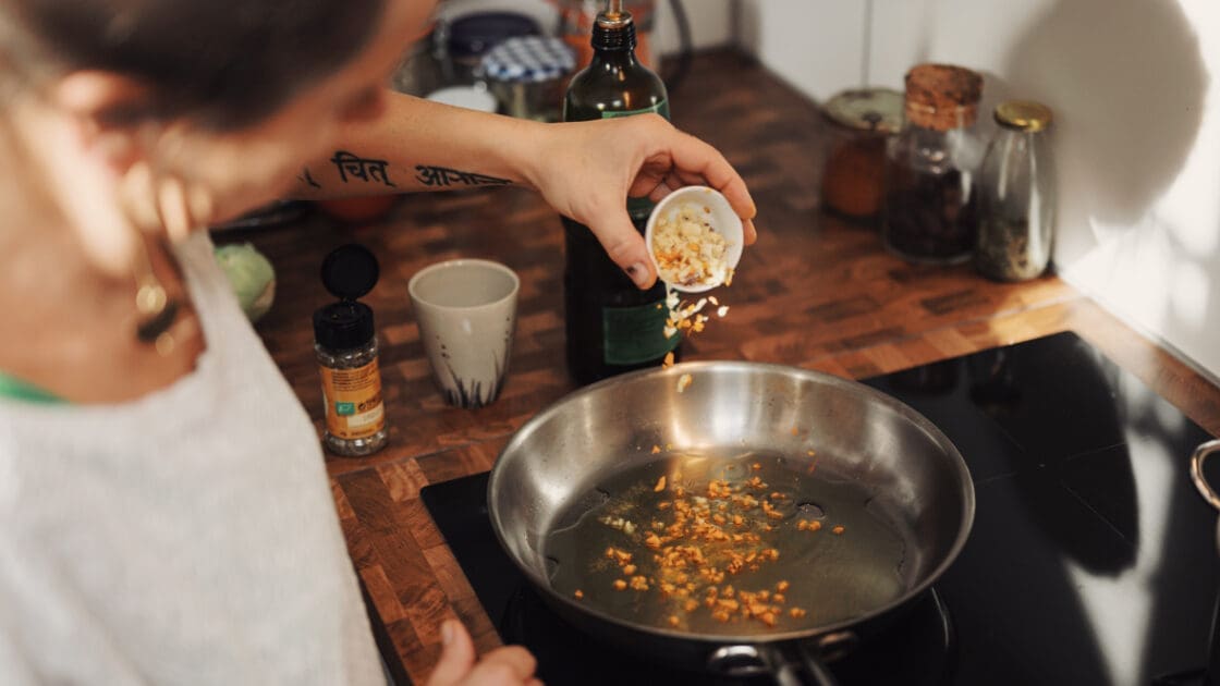 Woman pouring chopped garlic into saute pan.