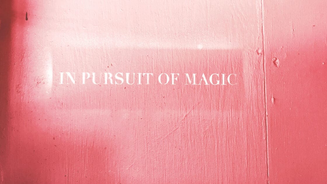 A pink wall with the words "in pursuit of magic" painted in white
