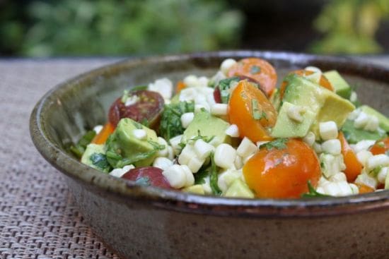 Image of a dark bowl of fresh corn, avocados, and tomatoes in a healthy avocado recipe