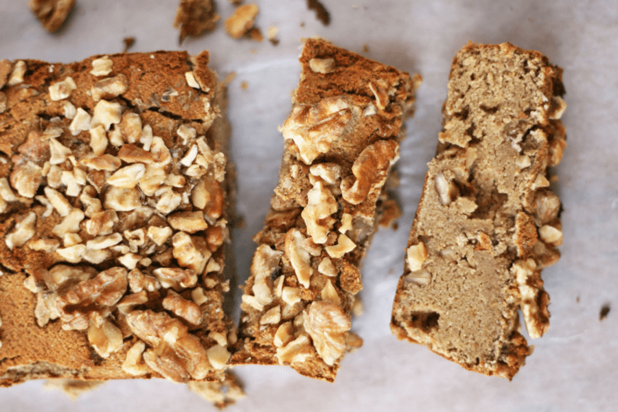 Image of paleo banana bread, overhead view with two pieces sliced off the loaf, on a piece of parchment paper with walnuts showing off the best banana bread recipe.
