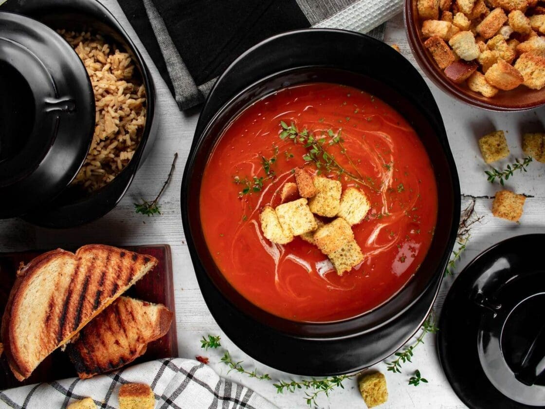Image of Xtrema stock pot with tomato soup with croutons and thyme served on a table with extra croutons in a bowl and grilled cheese on the side. Xtrema is safe nontoxic cookware with its pure ceramic cookware construction. Here are the best non toxic cookware options and safest cookware brands.