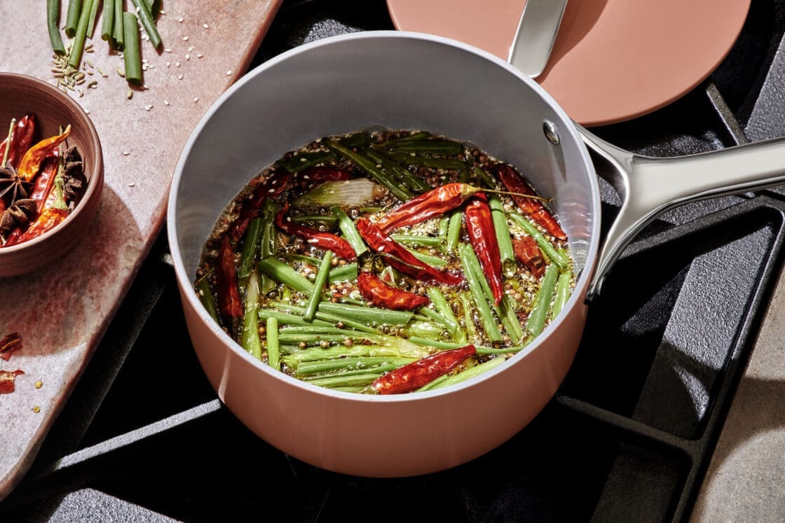 Image of a saucepan with red chilis, green onions, and soy sauce. The pan in a pretty pink color and it's being used for a Caraway pans review where a chef tests Caraway Cookware Sets
