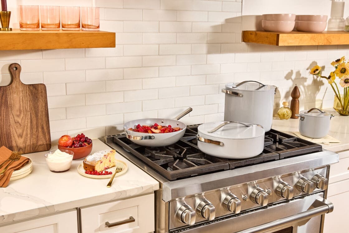 Image of a gray Caraway Cookware Set, Caraway reviews, caraway pots and pans review on a stove top with a white subway tile backsplash. Caraway Cookware Set, Caraway reviews, caraway pots and pans review,