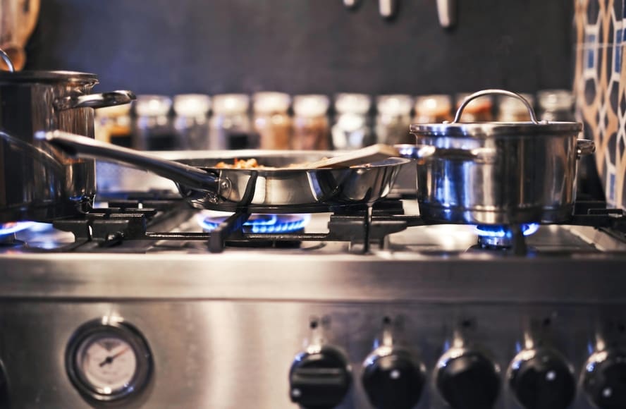 Image of a set of stainless steel pots and pans on a gas stovetop.