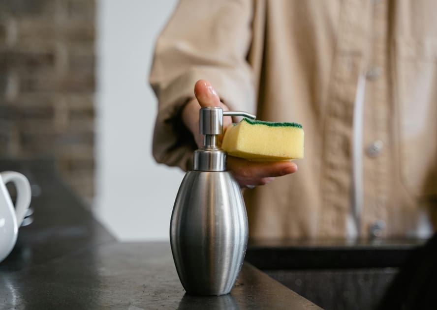 Image of a person dispensing soap from a soap dispenser onto a sponge.