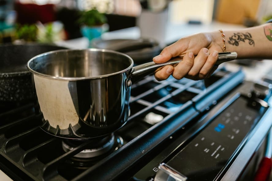 Is stainless steel cookware safe? An image of a person with a tattooed arm handling a stainless steel pot on a stovetop.