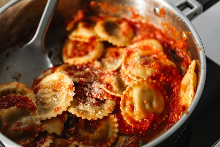 Image of ravioli with tomato sauce and parmesan in a stainless steel pot.