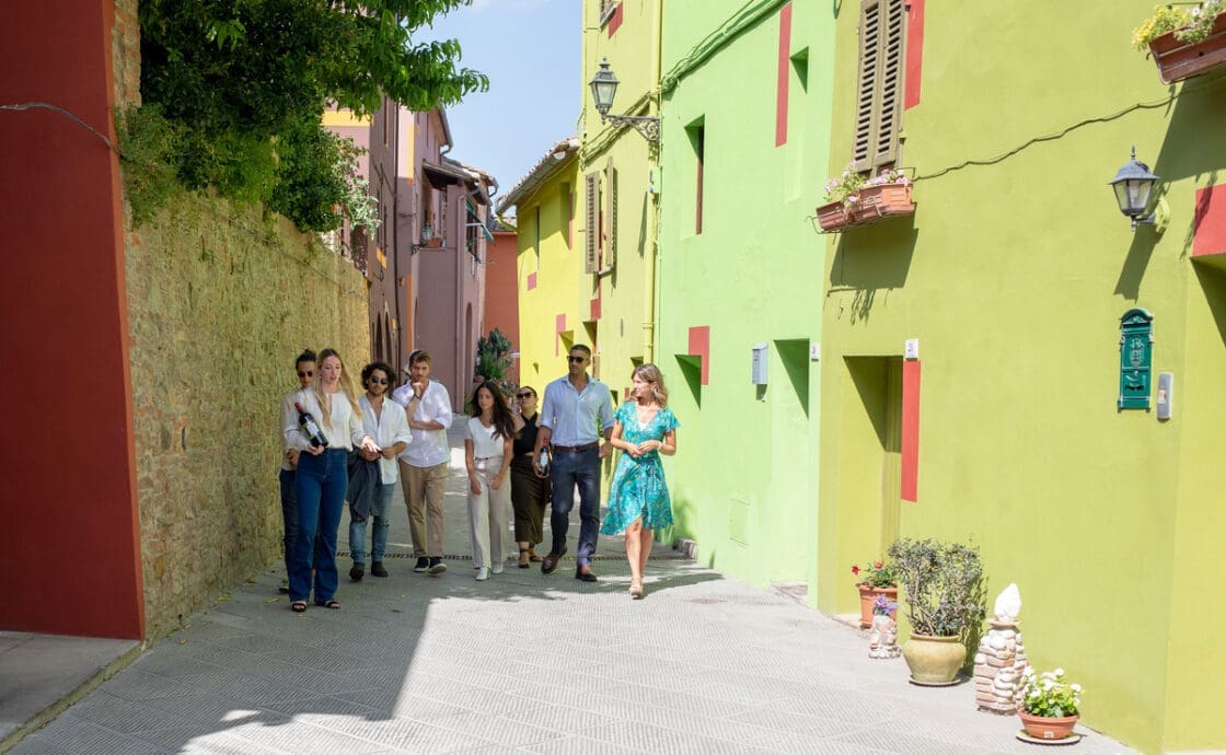 Image of a tour group of people standing in the Italian village Peccoli, and the Via de Mezzo that has turned the street into an open-air art museum with colorful walls.