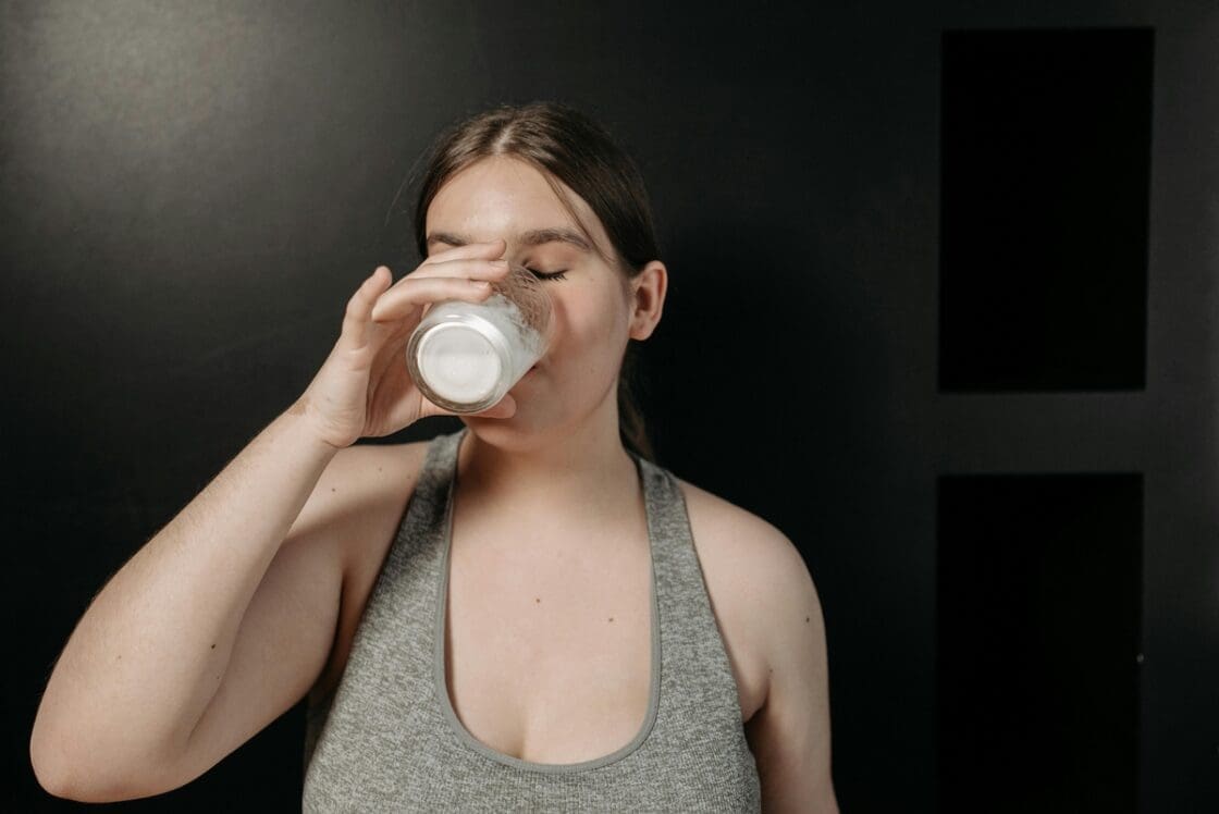 Image a young brunette woman drinking from a glass of milk with her eyes closed.