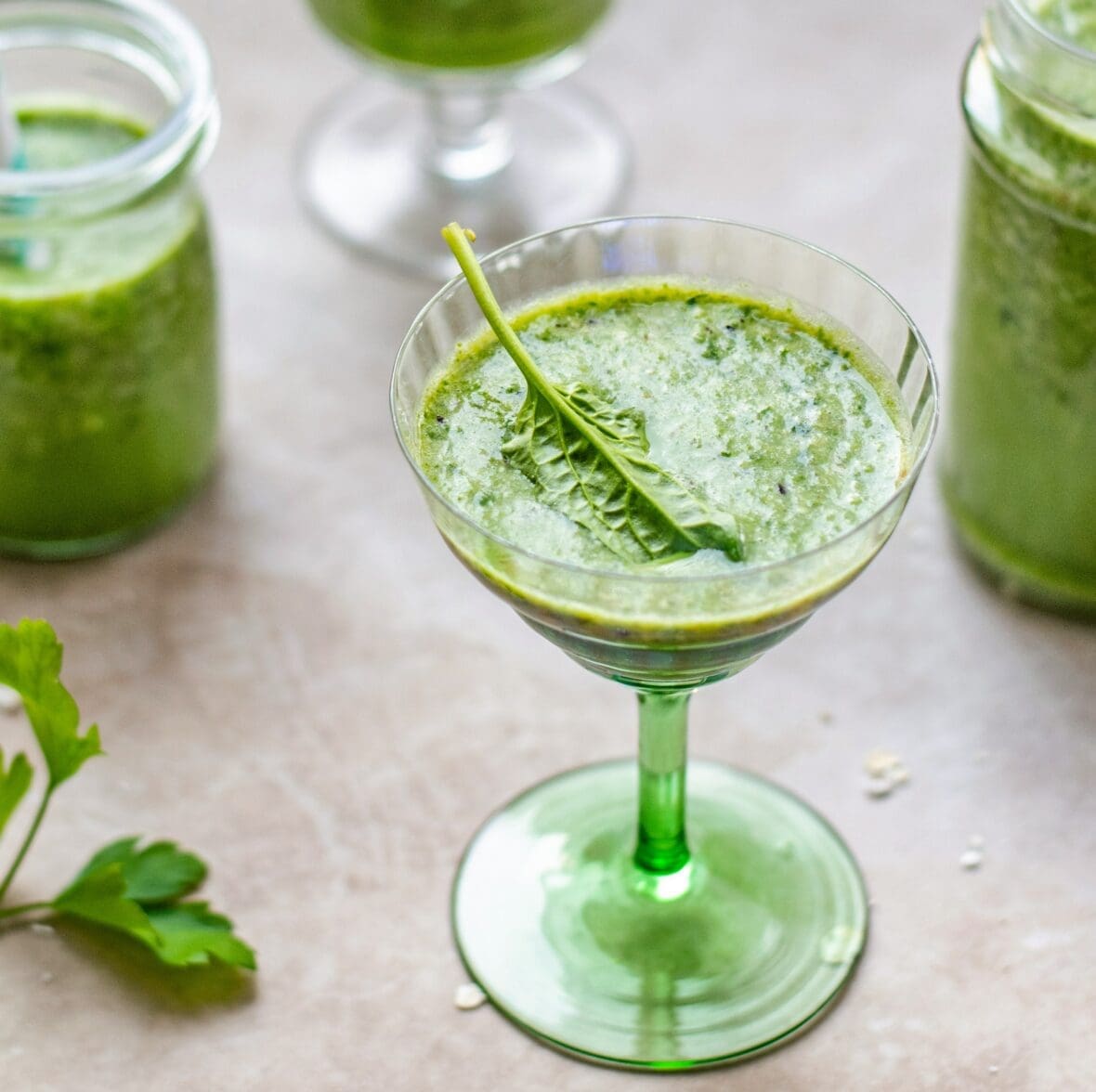 Image of a green juice drink in a coupe glass garnished with a single spinach leaf.