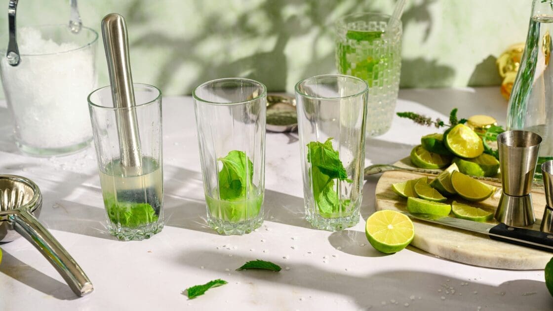 Image of green juice drinks being prepared in clear glasses with muddled mint