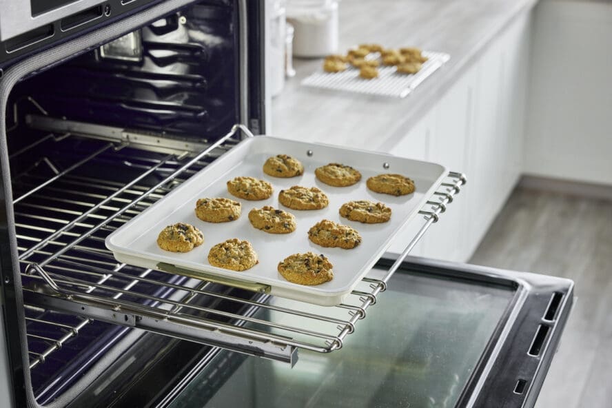 Image of the GreenPan half sheet baking pan in cream being slid out of the oven with rows of cookies.