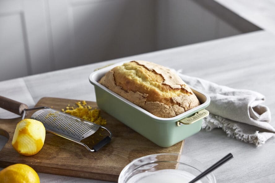 Image of the GreenPan Reserve loaf pan in sage green with a lemon loaf, alongside fresh lemon and a grater.