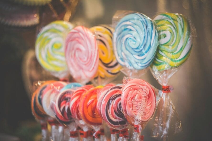 Image of a couple of rows of brightly colored lollipops, with a variety of artificial dyes.
