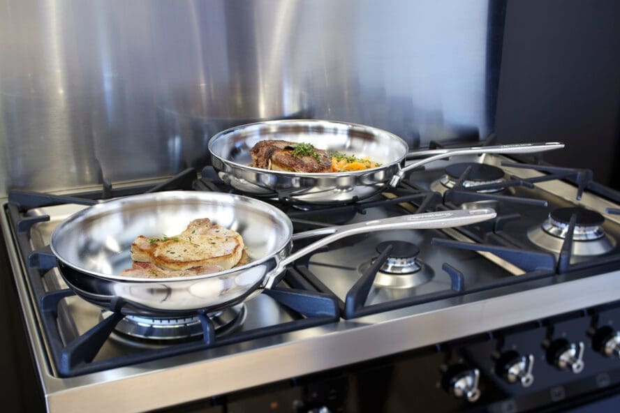Image of two stainless steel Demeyere sets shown searing proteins on a cooktop.