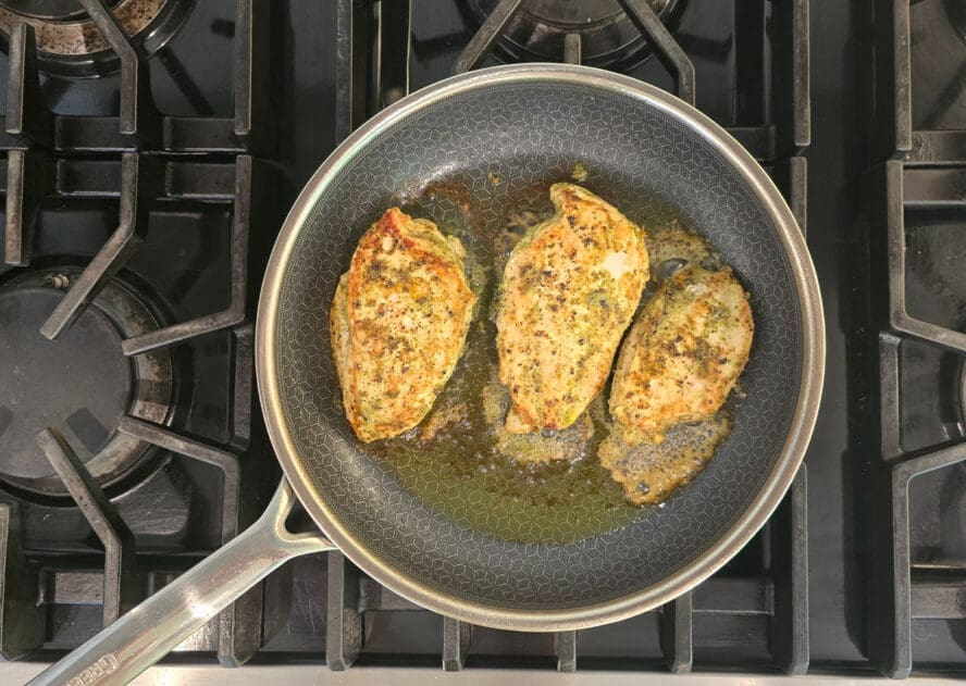Image of a GreenPan Spectra frypan on a stovetop being used to sear three chicken breasts to an appetizing golden brown color.