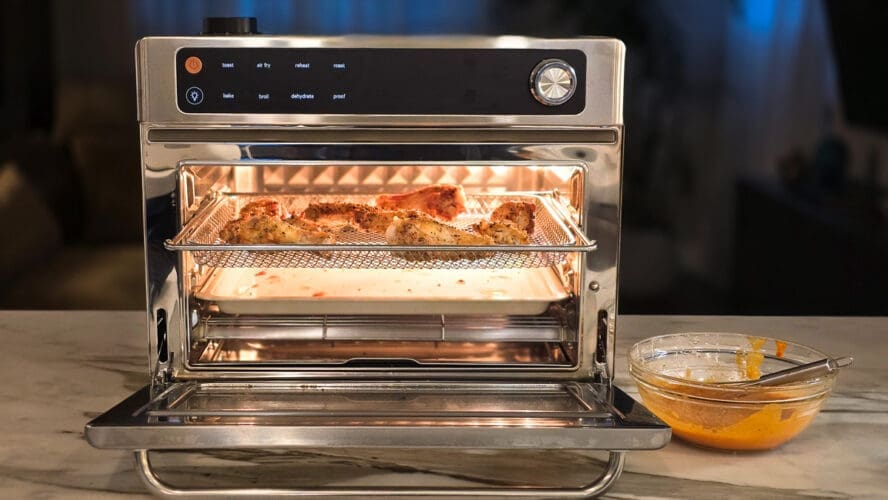 Image of the Our Place Wonder Oven Pro in stainless steel with chicken wings crisping up in the air fryer basket.