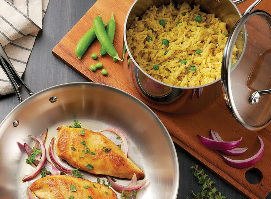 Image of a Tramontina stainless steel pan being used to sear proteins alongside a Tramontina saucepan filled with fluffy yellow rice.