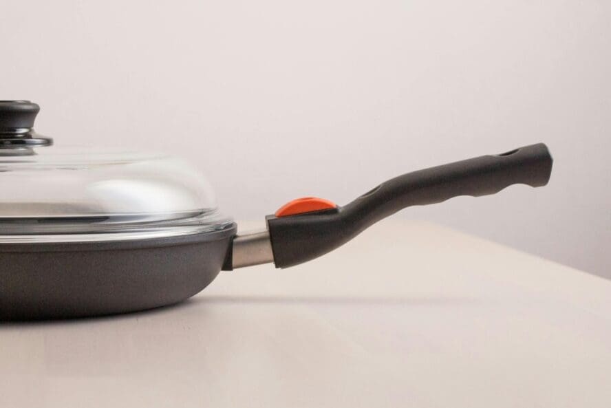 Image of a PFAS nonstick pan from a side view, showcasing the handle and its glass lid.