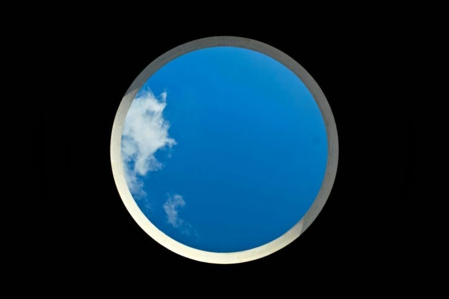Image of a circular window in a ceiling showcasing a bright blue patch of sky.
